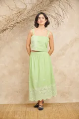 Conjunto de lino color verde claro, compuesto por un crop top con breteles y bordado de flores, y una falda midi con cintura elastizada y bordado de flores en el ruedo.