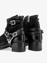 Bota corta de cuero negro, estilo motero, con caña arrugada y suela de plataforma gruesa con envoltura de cuero. Presenta una correa ajustable con hebilla y tachas metálicas alrededor del tobillo.