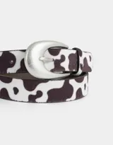 Cinturón de cuero sintético con estampado de vaca y hebilla metálica plateada.