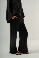 Pantalón negro de tiro alto con elástico en la cintura y pierna ancha. Presenta un pliegue marcado vertical en el frente de cada pierna.