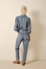 Jean de denim azul con lavado claro y efecto bigotes, tiro medio-alto y calce holgado con pierna recta que ajusta hacia el ruedo. Presenta bordado de alas en los bolsillos traseros.