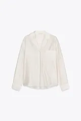 Camisa color crudo confeccionada en lyocell. Tiene cuello solapa, manga larga con puños y cierre frontal con botones. Cuenta con un bolsillo de plastrón con bordados a tono en el pecho.
