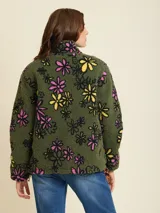 Campera verde militar de sherpa con estampado de flores en tonos rosa, amarillo y negro. Tiene cuello alto, cierre frontal y un bolsillo de nylon negro en el pecho con logo bordado.