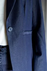 Blazer de tencel color azul marino con cuello de solapa y cierre frontal de un solo botón. Presenta bolsillos delanteros simulados con detalle de vivo trenzado y un diseño estructurado de calce entallado.