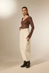 Pantalón jean color blanco, de corte barrel y tiro bajo, con detalles de tachas metálicas en los bolsillos delanteros y a lo largo de las costuras laterales.