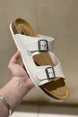 Sandalias blancas de cuero con doble tira y hebillas metálicas ajustables. Suela anatómica de corcho y goma.
