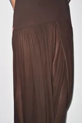 Vestido largo color marrón oscuro, con cuello halter que forma un drapeado en el busto. La parte superior es ajustada y la falda es larga con un panel inferior fruncido y drapeado en tela más liviana.