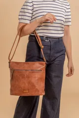 Cartera tipo bandolera de tamaño mediano confeccionada en símil cuero color marrón. Presenta una correa larga regulable, dos compartimientos principales y un bolsillo frontal con cierre de cremallera.