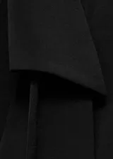 Vestido corto negro con cuello camisero, escote en V cruzado, mangas largas con puños abotonados, lazo desmontable en el cuello y detalle de pliegues en la cintura.