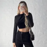 Top corto negro de terciopelo, con cuello alto y mangas largas de tul con lunares plateados.