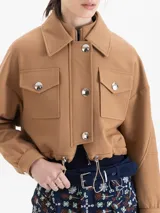 Chaqueta corta color marrón, sin forrar, confeccionada en sarga. Presenta doble cuello (mao interno y camisero externo), doble acceso frontal con cierre y broches, bolsillos plaqué con tapa y jareta con elástico y tancas metálicas. Las mangas tienen recortes y puños con broches.