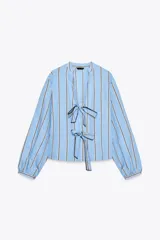 Camisa celeste con rayas verticales marrones y blancas, cuello redondo con escote en pico y mangas largas abullonadas. Cierre frontal con lazos con pespuntes marcados.