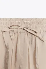 Pantalón de tiro medio color beige, con cintura elástica ajustable con cordones, bolsillos delanteros y puños elásticos en los tobillos.