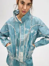 Campera rompevientos estilo biker con capucha desmontable, color celeste con estampado de nubes blancas y detalles en blanco.