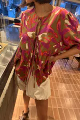 Blusa de calce holgado con estampado floral en tonos marrones, fucsias, naranjas y blancos. Escote en V con doble lazo ajustable y mangas 3/4 con volumen.