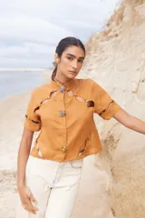 Blusa color camel con cuello mao, cierre frontal con botones y aberturas geométricas en hombros, mangas y cintura.