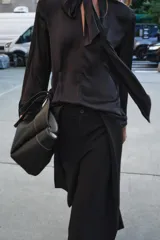 Blusa negra de cuello redondo con lazo en el mismo tejido. Manga larga acampanada y bajo recto.