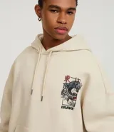 Hoodie color beige claro, corte boxy, con capucha ajustable y bolsillo canguro. Presenta un gran estampado gráfico en la espalda con un dragón oriental, texto en inglés y caracteres japoneses, y la palabra "BRAVE" en la parte superior.