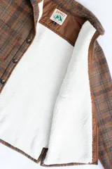 Camisa leñadora a cuadros marrón y naranja, forrada en corderito sintético, con cuello clásico, cierre frontal con botones, dos bolsillos frontales con tapa y puños abotonados.