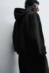 Sudadera negra con capucha, corte boxy, cierre frontal con cremallera, bolsillos laterales y puños elásticos.