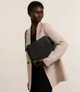 Bolso mediano tipo postman color negro con textura en relieve de líneas horizontales. Tiene correa larga regulable, cierre con cremallera y forro de poliéster.