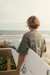 Remera verde con estampa en la espalda con texto "Glassy Waves Club" y dibujo de palmeras y una ola.