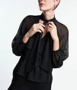 Blusa negra de chiffon con cuello alto con lazo, mangas largas con puños ajustados, detalle de volado delantero y volado en encaje.