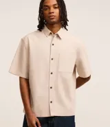 Camisa beige de algodón texturizado, corte boxy, manga corta, cuello inglés y abotonadura frontal.