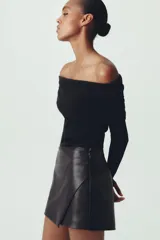Falda pantalón corta negra de cuero sintético, tiro medio y corte cruzado.