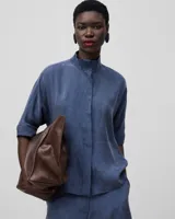 Camisa azul de lyocell, de corte holgado, con cuello mao, manga corta japonesa y botonadura frontal oculta.