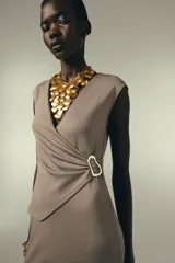 Vestido midi color beige, de corte recto, con escote en pico cruzado, sin mangas y detalle de hebilla metálica en la cintura.