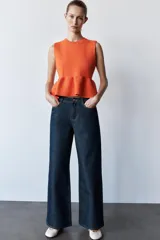 Top tejido de punto color naranja, de cuello redondo y sin mangas. Tiene corte ajustado en el torso y peplum en la cintura.