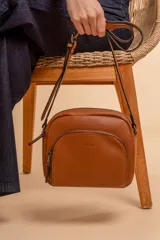 Bandolera color marrón de cuero sintético con correa regulable, cierre superior y bolsillo frontal con cierre.