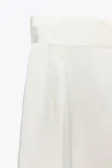 Pantalón blanco de tela satinada, tiro alto, corte ancho y pliegues en la parte delantera y trasera.