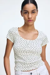 Remera blanca con estampado de flores pequeñas en negro, escote cuadrado y tapeta de botones. Corte entallado y mangas cortas.