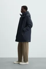 Parka azul marino de corte recto, con capucha y cuello alto desmontable. Interior acolchado, cierre frontal con cremallera oculta y botones a presión, bolsillos laterales y puños de rib.