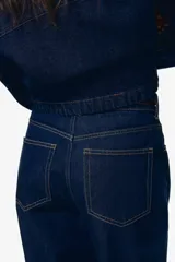 Pantalón de jean azul oscuro de tiro alto, corte recto y pierna ancha. Diseño de cinco bolsillos con costuras a la vista. Inspirado en los años 70.