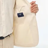 Blazer color beige de lino, corte slim, con solapa de muesca, cierre de dos botones, bolsillo en el pecho y bolsillos delanteros con solapa.