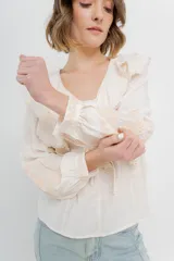 Blusa color crema con volados en el frente, detalle de puntilla y bordados florales en mangas.