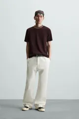 Pantalón negro de algodón con corte relajado y pierna ancha (flare fit). Presenta cierre frontal con botón y cremallera, bolsillos delanteros y bolsillos traseros de plastrón.