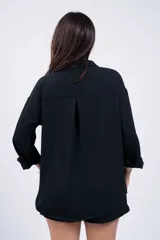 Camisa negra de corte amplio, con cuello clásico, cierre frontal con botones, manga larga con puños arremangados y bolsillo de parche en el pecho.