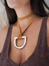 Collar con tira de cuero color suela y dije metálico dorado en forma de estribo.