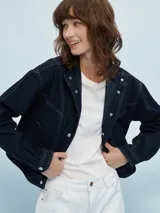 Campera corta de jean azul oscuro con costuras en hilo color crema, cuello mao y cierre con botones metálicos.