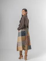 Camisa de corte clásico, color marrón oscuro con brillo sutil dorado, confeccionada en tela nacarada. Presenta apliques de flores tridimensionales fruncidas en el área del pecho.