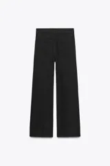 Pantalón de jean negro de corte palazzo, tiro medio y cintura con trabillas. Tiene bolsillos delanteros y traseros, raya planchada en el frente y cierre frontal con cremallera, botón y ganchos metálicos.