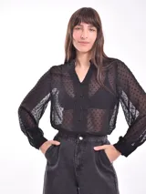 Camisa negra traslúcida con lunares, cuello en V con volados y botones frontales.