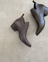 Botín de cuero color marrón claro, con punta fina, cierre lateral con cremallera dorada, detalle de pespuntes en el empeine y taco cuadrado de madera color negro.