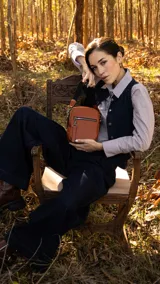 Bandolera de cuero sintético en color marrón claro con apertura superior de cierre. Presenta un bolsillo frontal con cierre y una correa de galón ajustable y desmontable con diseño a rayas. El interior incluye un bolsillo de fácil acceso.