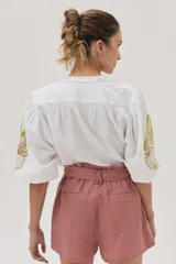Camisa blanca de mezcla lino-algodón, con corte recto y mangas clásicas. Presenta un bordado floral en el hombro con distintas técnicas y canutillos.