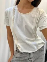 Remera blanca con detalles en puntilla y combinaciones de telas, de corte cómodo y manga corta.